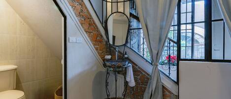 Une salle de bain avec des toilettes, un lavabo avec un miroir et une fenêtre avec des rideaux.