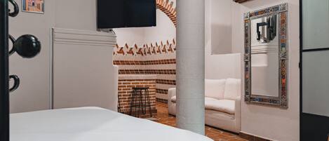 Habitación de hotel con cama, televisor montado en la pared, sofá blanco y espejo estampado.