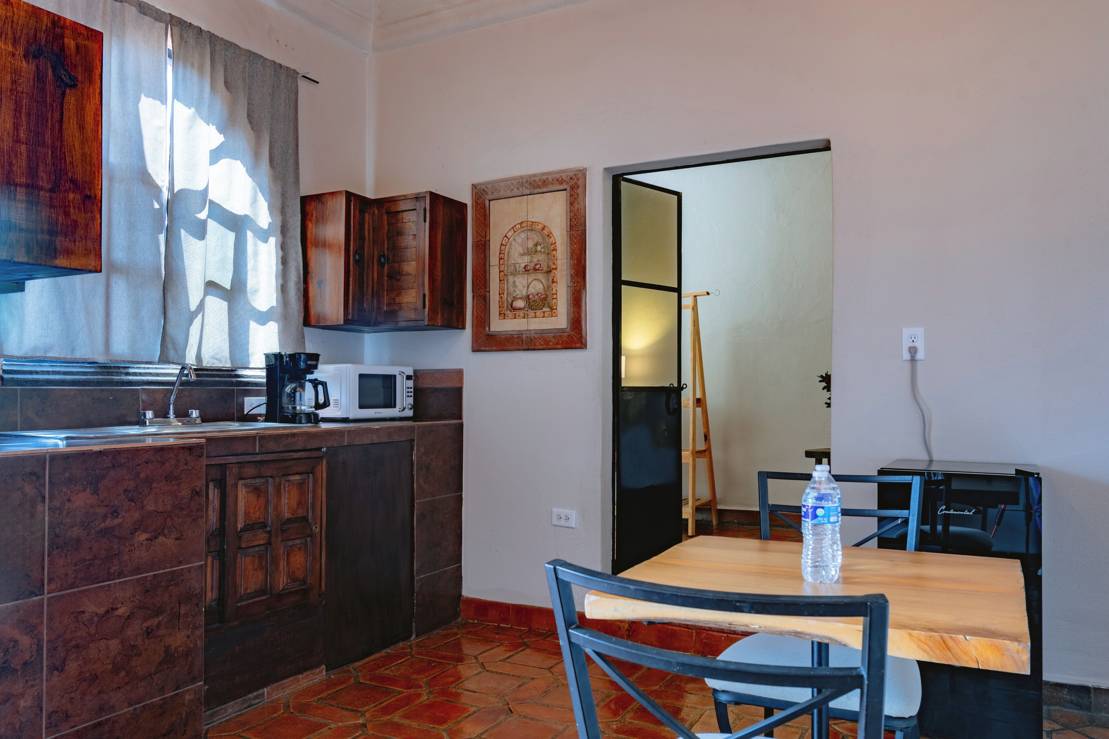 A kitchen with dark wooden cabinets, a microwave, and a coffee maker on the counter. There is a table with chairs and a water bottle on it.