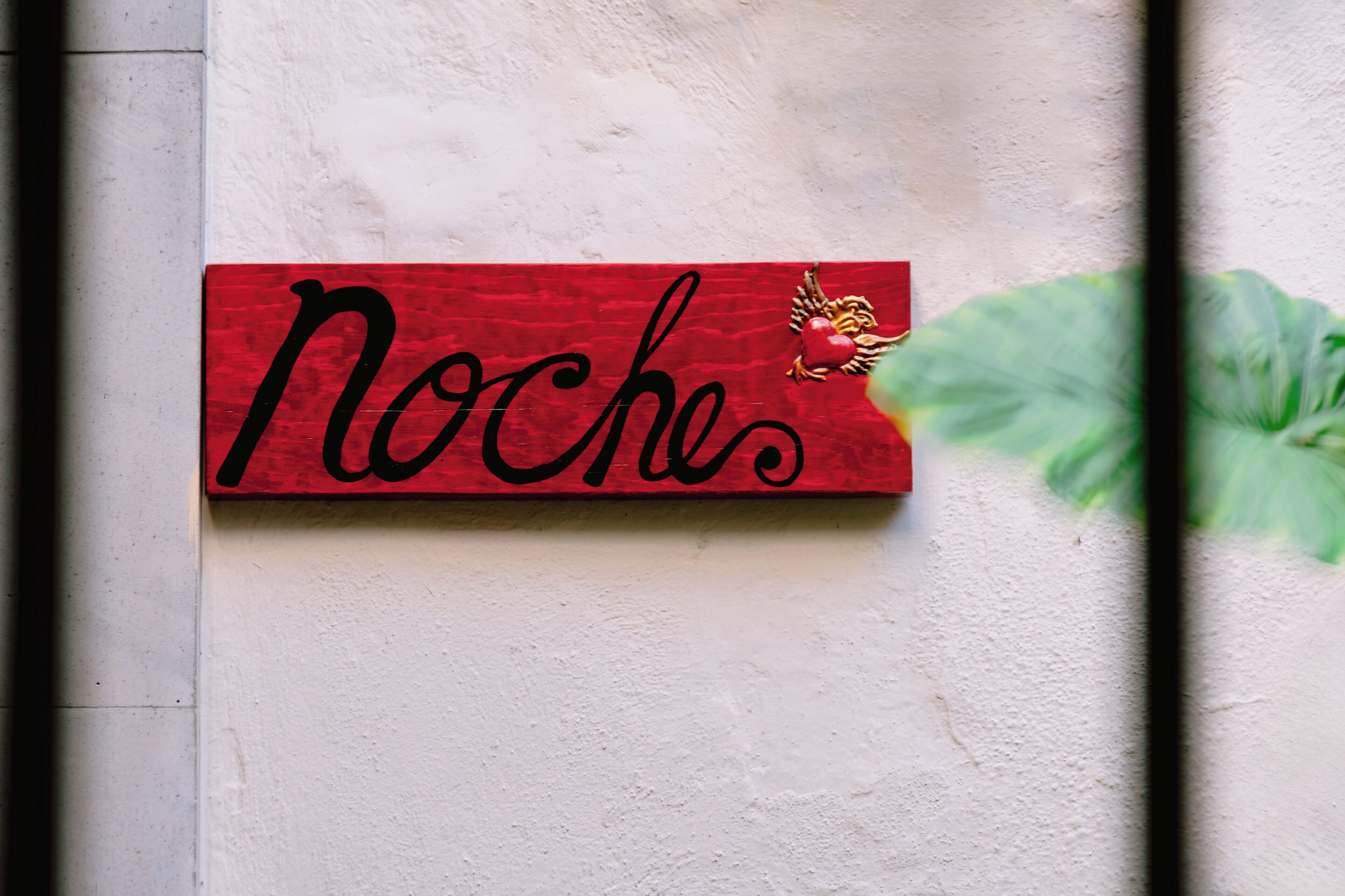 Ein rotes Schild mit dem Wort 'Noches' und einem dekorativen Element an einer Wand.