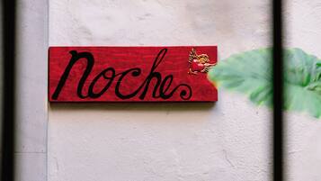 Ein rotes Schild mit dem Wort 'Noches' und einem dekorativen Element an einer Wand.