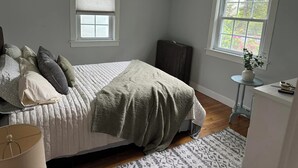 Una camera da letto con un letto, un comodino, una lampada, una finestra con persiane e un tavolino con una pianta.