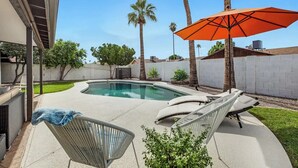 Um quintal com piscina, cadeiras de descanso e um guarda-sol laranja.