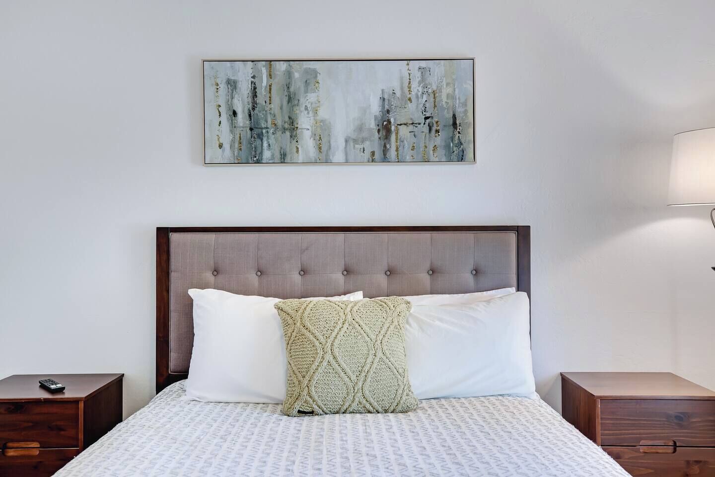 A neatly made bed with a tufted headboard, a plain white pillow, a textured throw pillow, and a patterned bedspread.