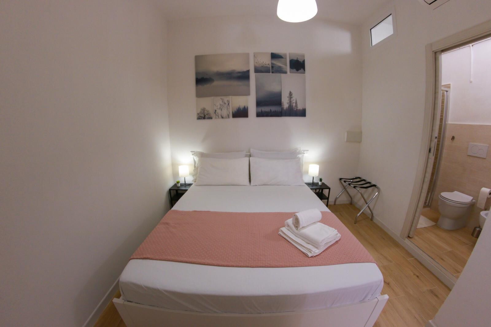 Ein ordentlich eingerichtetes Hotelzimmer mit Bett, Nachttischen, einem kleinen Schreibtisch, einem Sessel und einem Badezimmer.