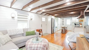 A spacious living room with a sofa, a coffee table, and a dining area with a table and chairs. - Enchanting 2 Bedroom Cottage, The Fox Den, 258 Acres, Farmville, VA (Rice)