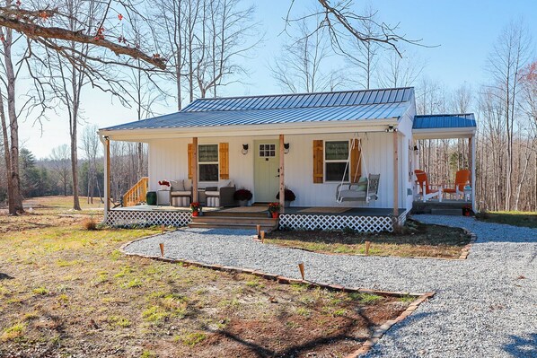 A cabin with a covered porch, a swing chair, and a seating area with chairs and a table. - Enchanting 2 Bedroom Cottage, The Fox Den, 258 Acres, Farmville, VA (Rice)