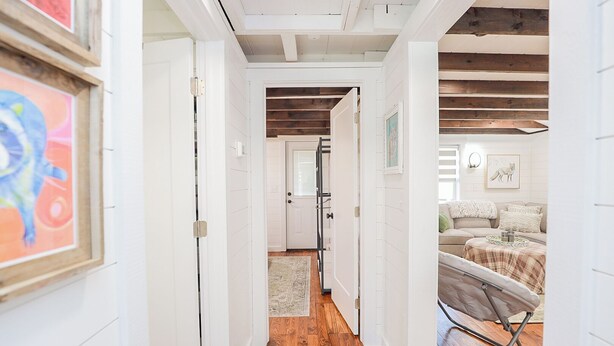 A narrow hallway with white walls and wooden beams, leading to a room with a sofa and a small table. - Enchanting 2 Bedroom Cottage, The Fox Den, 258 Acres, Farmville, VA (Rice)