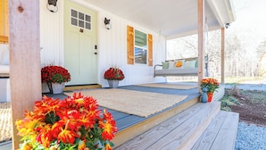 A porch with a wooden bench, two potted plants with red flowers, and a cat-shaped decoration on the wall. - Enchanting 2 Bedroom Cottage, The Fox Den, 258 Acres, Farmville, VA (Rice)