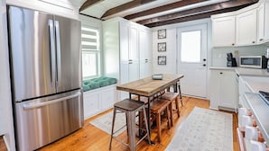 A modern kitchen with stainless steel appliances, wooden beams, white cabinetry, and a dining area with stools. - Enchanting 2 Bedroom Cottage, The Fox Den, 258 Acres, Farmville, VA (Rice)