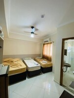 Quarto de hotel com duas camas de solteiro, ventoinha no teto, ar condicionado e casa de banho visível através de uma porta de vidro.
