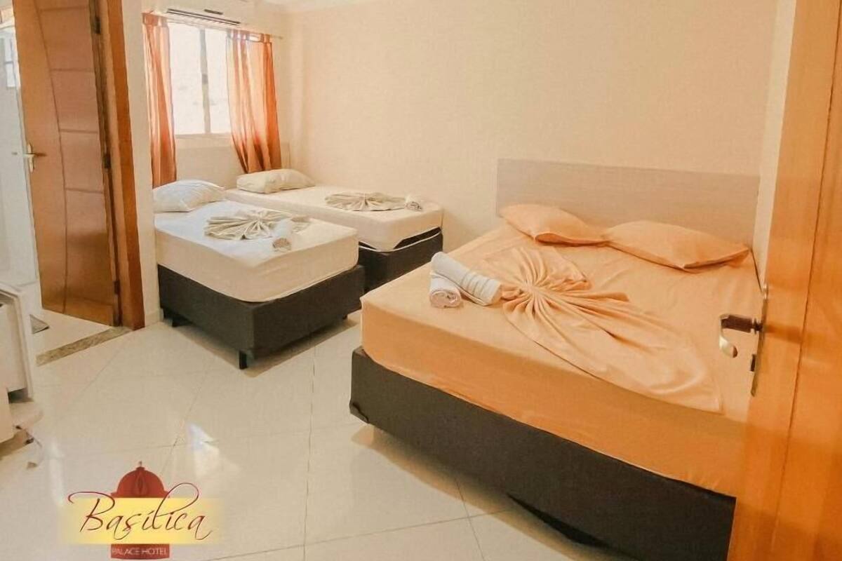 Habitación de hotel con dos camas, ventilador de techo y ventana con cortinas.