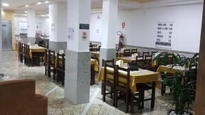 A spacious dining area with marble flooring, multiple tables with yellow tablecloths, and potted plants. - Basilica Palace Hotel (Aparecida)