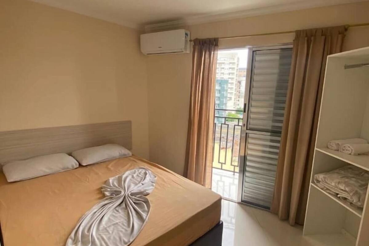 Una habitación de hotel con cama, armario, aire acondicionado y balcón con cortinas.