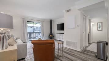 Una sala de estar con sofá, un reposapiés marrón, chimenea, televisión y una mesita.