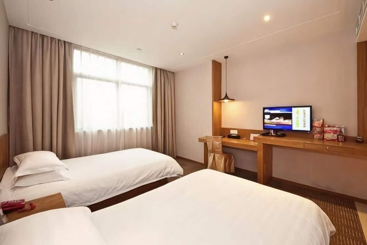 Une chambre d’hôtel avec deux lits, un bureau avec une télévision et une fenêtre avec des rideaux.