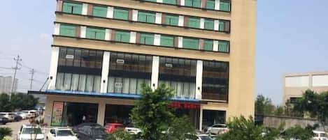 Un hotel de varios pisos con fachada plana, grandes ventanales y un estacionamiento al frente.