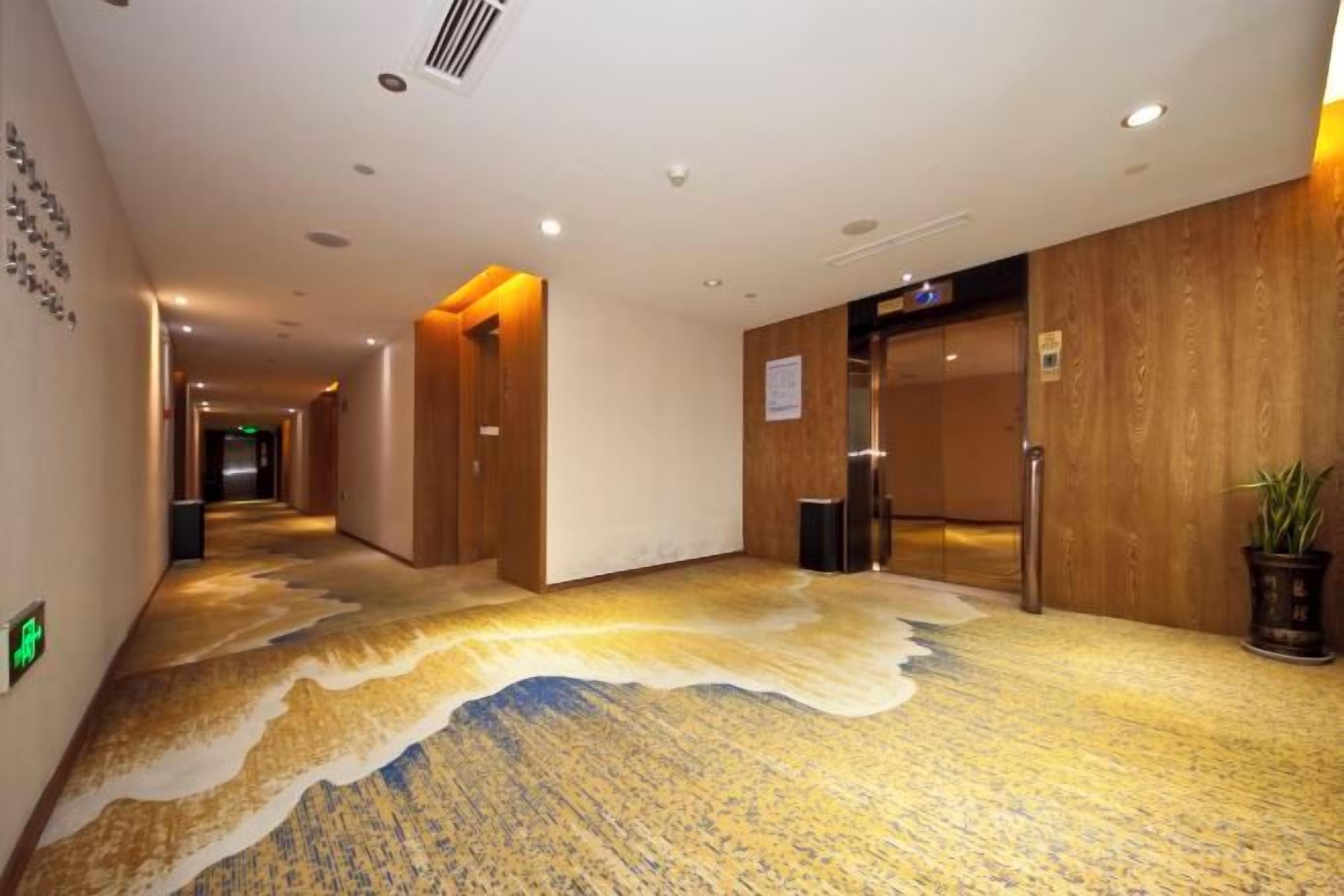 A hotel corridor with a patterned carpet, wooden walls, and a potted plant.
