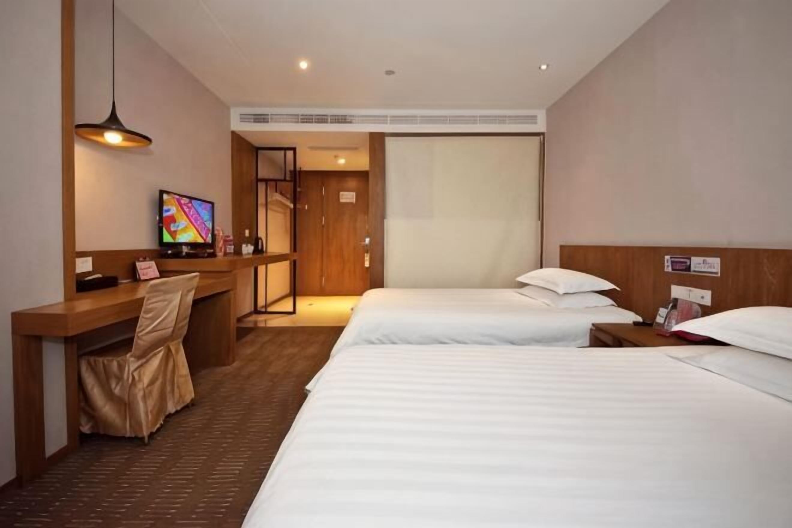 Ein Hotelzimmer mit Schreibtisch, zwei Betten, Fernseher und Duschbereich.