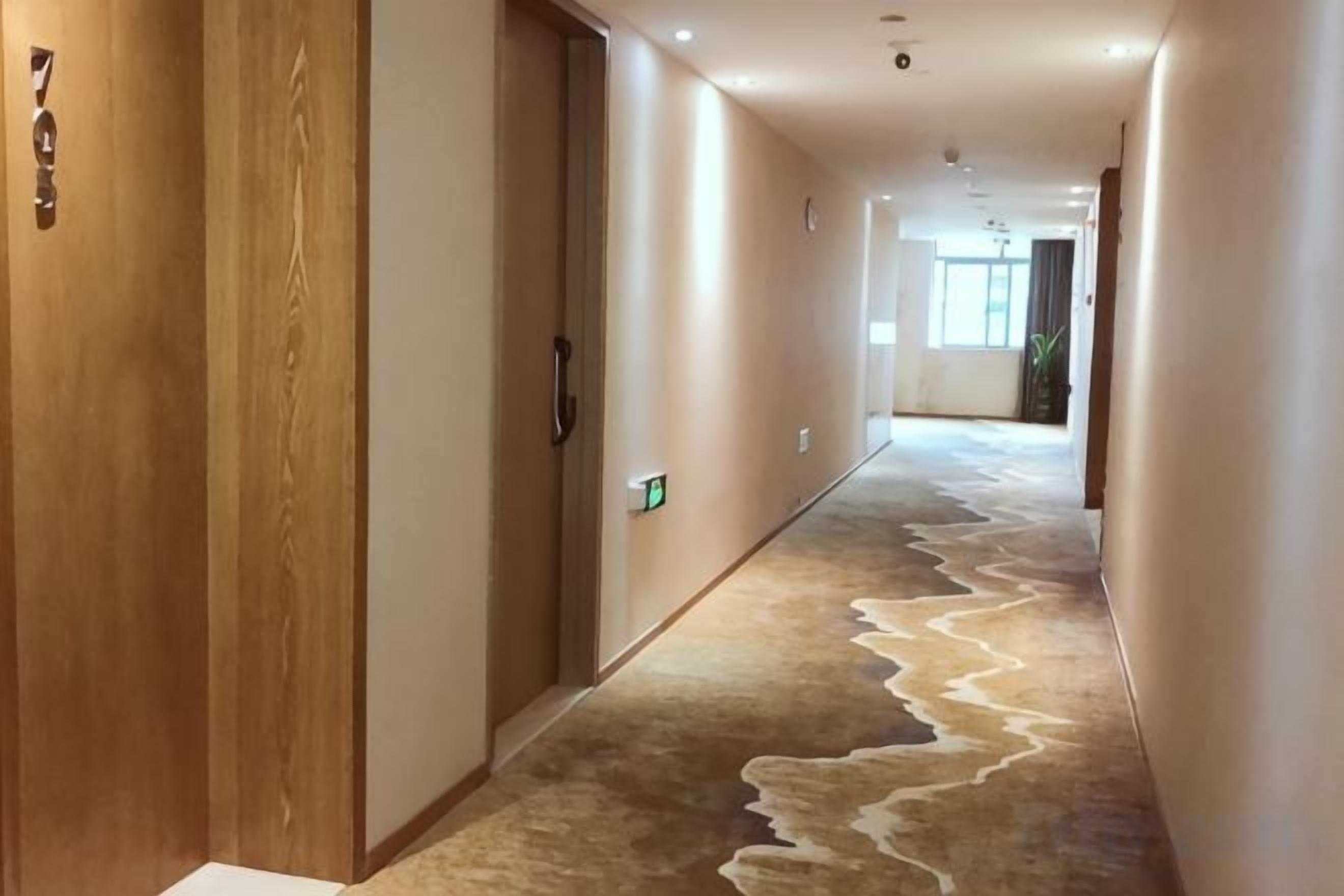 A hotel hallway with a carpeted floor, wooden doors, and a light switch on the wall.