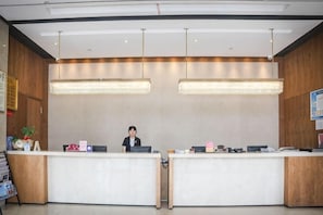 Un comptoir d’accueil avec deux réceptionnistes, un mur en bois et des luminaires suspendus.