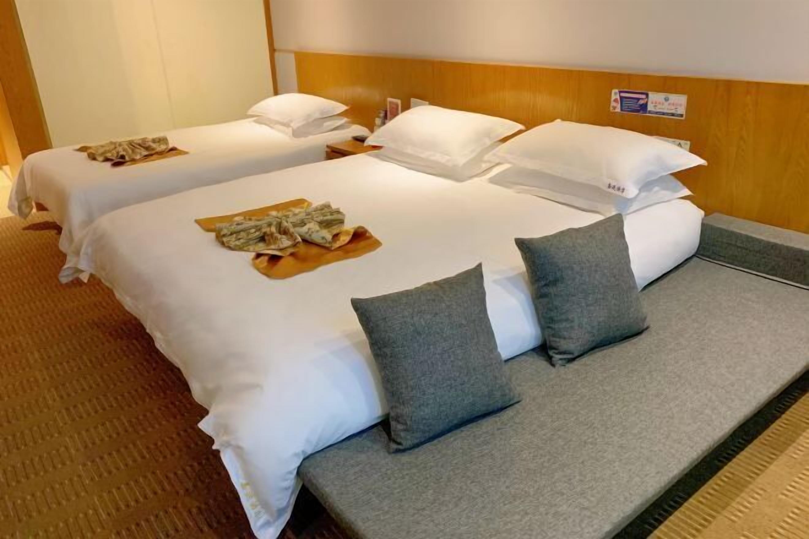 A hotel room with two single beds, each with white linens and pillows, and a grey sofa bed.