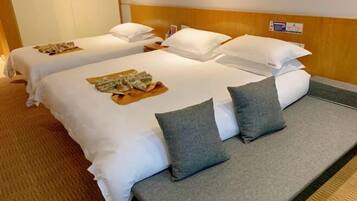 A hotel room with two single beds, each with white linens and pillows, and a grey sofa bed.