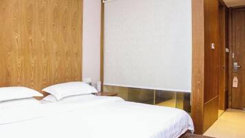 A hotel room with a wooden wall, a large bed with white bedding, a window with a blind, and a wooden door.