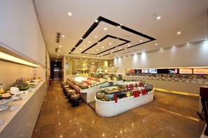 Amplio espacio interior con una exhibición central de diversos alimentos, una larga barra con caja registradora y un diseño de techo moderno.