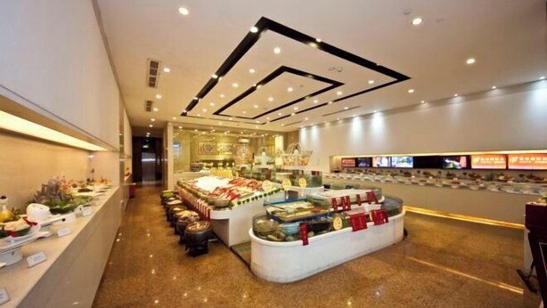 Eine moderne Hotelhalle mit einer zentralen Speisenauslage, einer langen Rezeption und einem sauberen, glänzenden Boden.