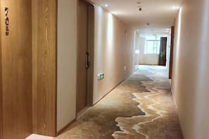 A hallway with a carpeted floor, wooden doors, and a light switch on the wall. - WENZHOU JIAYAN HOTEL (Wenzhou)