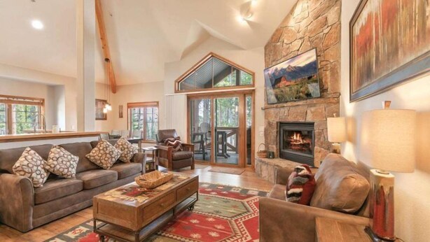 A spacious living room with a stone fireplace, a large window, and a cozy seating area. - Premier 2 Bedroom Townhome Across From Snowflake Lift - Walk to Lifts (Breckenridge)