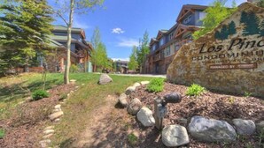 A residential area with a large sign for Los Piños Condominium, featuring a stone pathway, trees, and modern buildings. - Premier 2 Bedroom Townhome Across From Snowflake Lift - Walk to Lifts (Breckenridge)