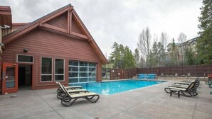 A building with a red exterior and a swimming pool. There are lounge chairs around the pool. - Premier 2 Bedroom Townhome Across From Snowflake Lift - Walk to Lifts (Breckenridge)