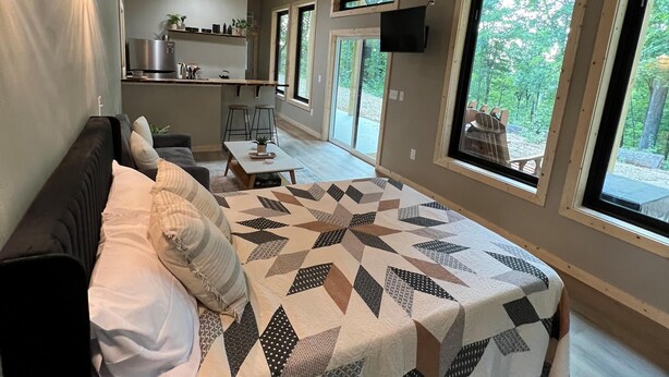 Ein Schlafzimmer mit Bett, Deckenventilator, Fernseher und großen Fenstern.