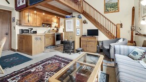A cozy living area with a wooden staircase, a kitchen with wooden cabinets, a television, and a sofa. - Opera House Loft 02 - Bethel Village (Bethel)