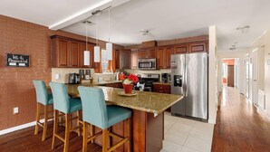 A modern kitchen with a central island, bar stools, stainless steel appliances, and a brick accent wall.