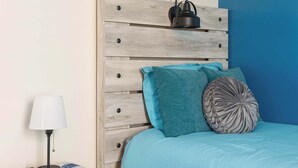A bedroom with a wooden headboard, a teal bedspread, and a bedside table with a lamp.