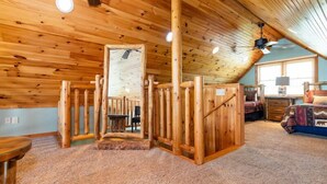 Interno di una baita con una scala in legno, una ventola a soffitto, un letto e una finestra.