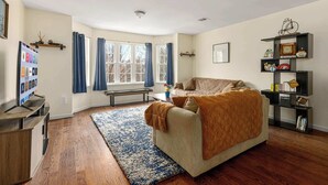 Una sala de estar con sofá, una mesa de centro, una estantería, una ventana con cortinas y piso de madera.