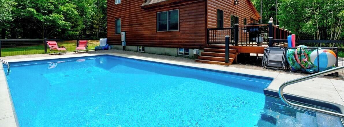 Ein Swimmingpool mit Holzterrasse, Liegestühlen und einer Holzhütte.