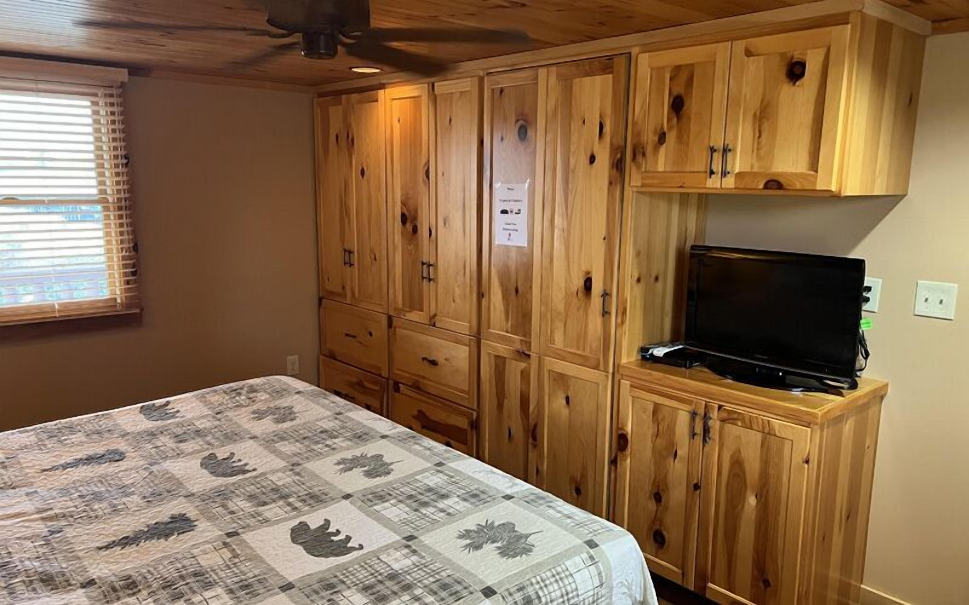 A bedroom with a bed, wooden cabinets, and a television.