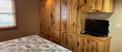 A bedroom with a bed, wooden cabinets, and a television.