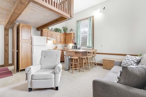 A compact living space with a kitchenette, a dining area with bar stools, a sofa, and a chair. - Opera House Loft 03 - Bethel Village (Bethel)