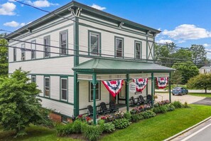 A two-story building with a porch, green trim, and a sign indicating it is an opera house. - Opera House Loft 03 - Bethel Village (Bethel)