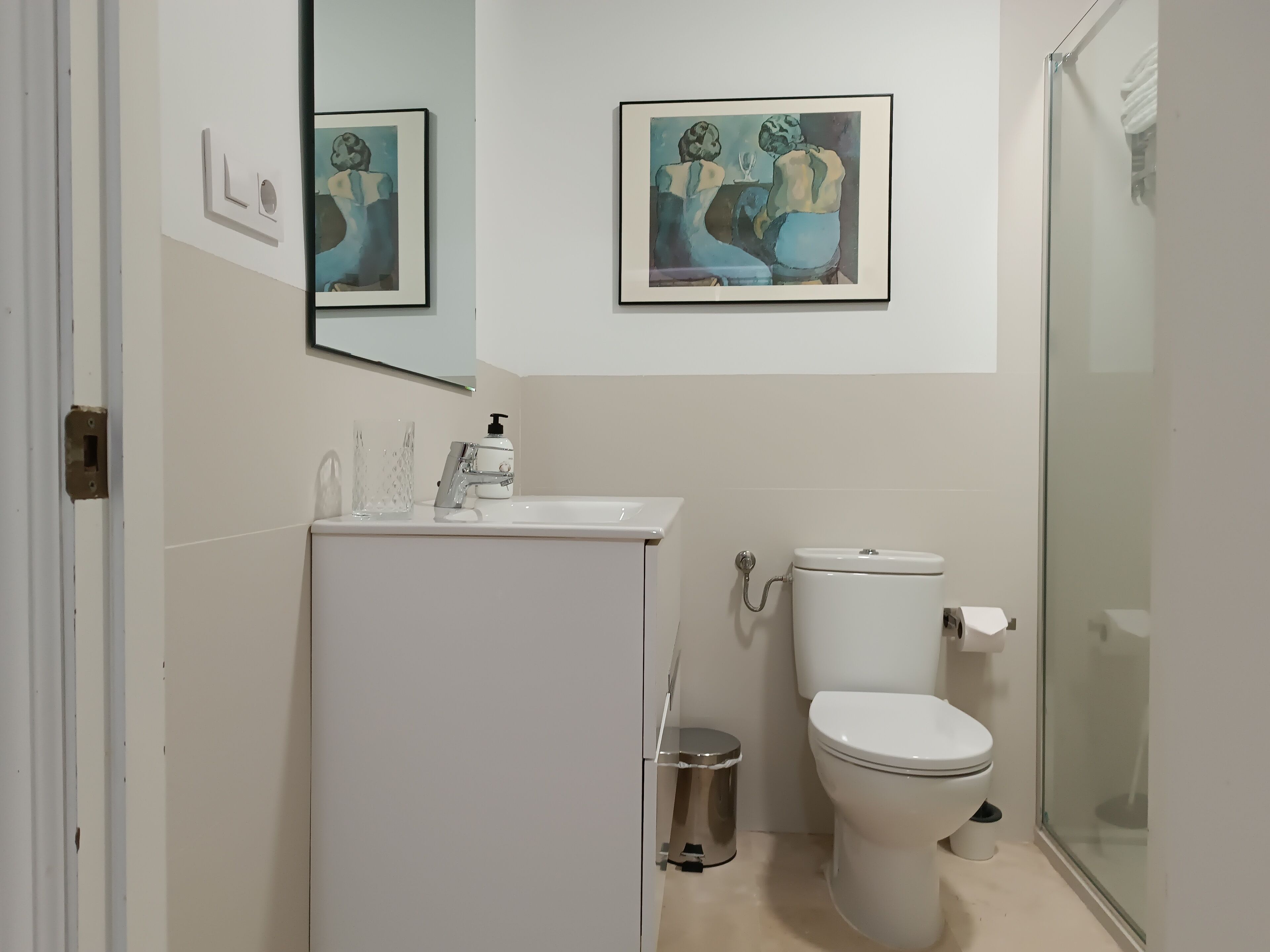 Un baño moderno con inodoro, lavamanos y cabina de ducha de vidrio. Hay dos obras de arte enmarcadas en la pared.