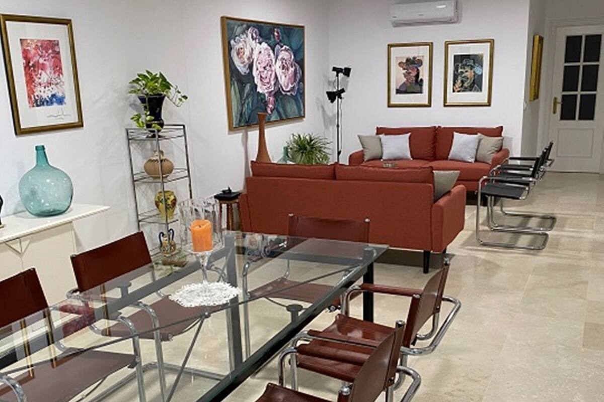 A modern dining area with a glass table and metal chairs, a red sofa, and artwork on the walls.