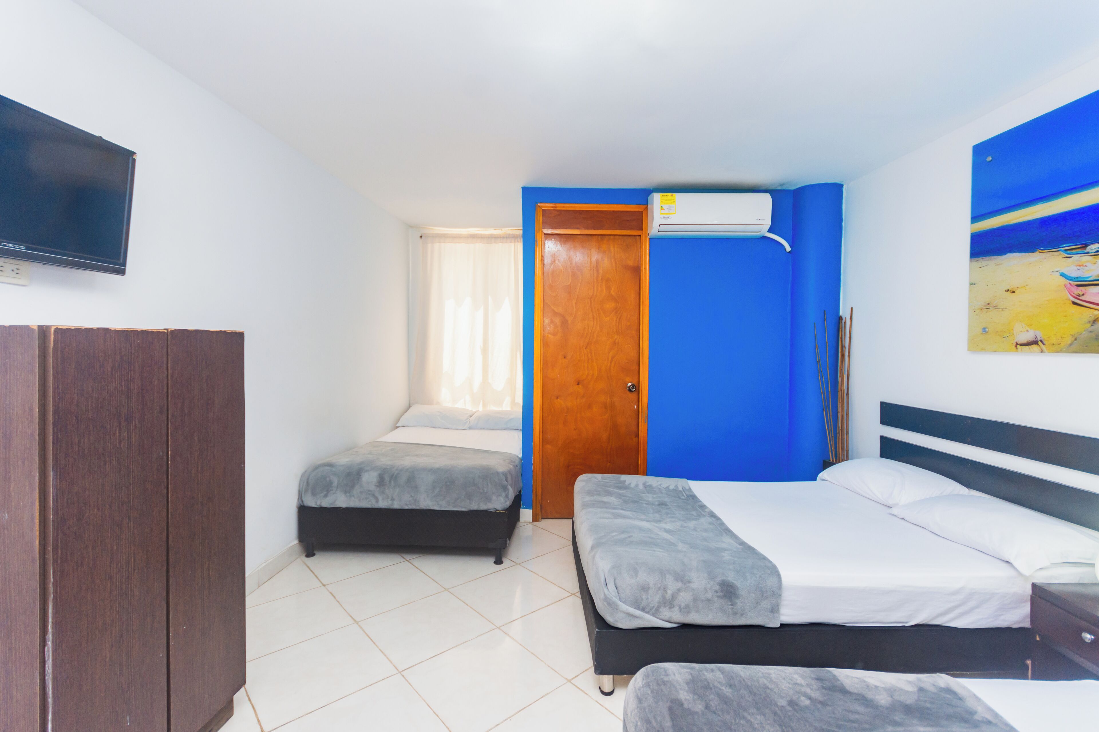 A bedroom with two beds, a wardrobe, a TV, and an air conditioner.