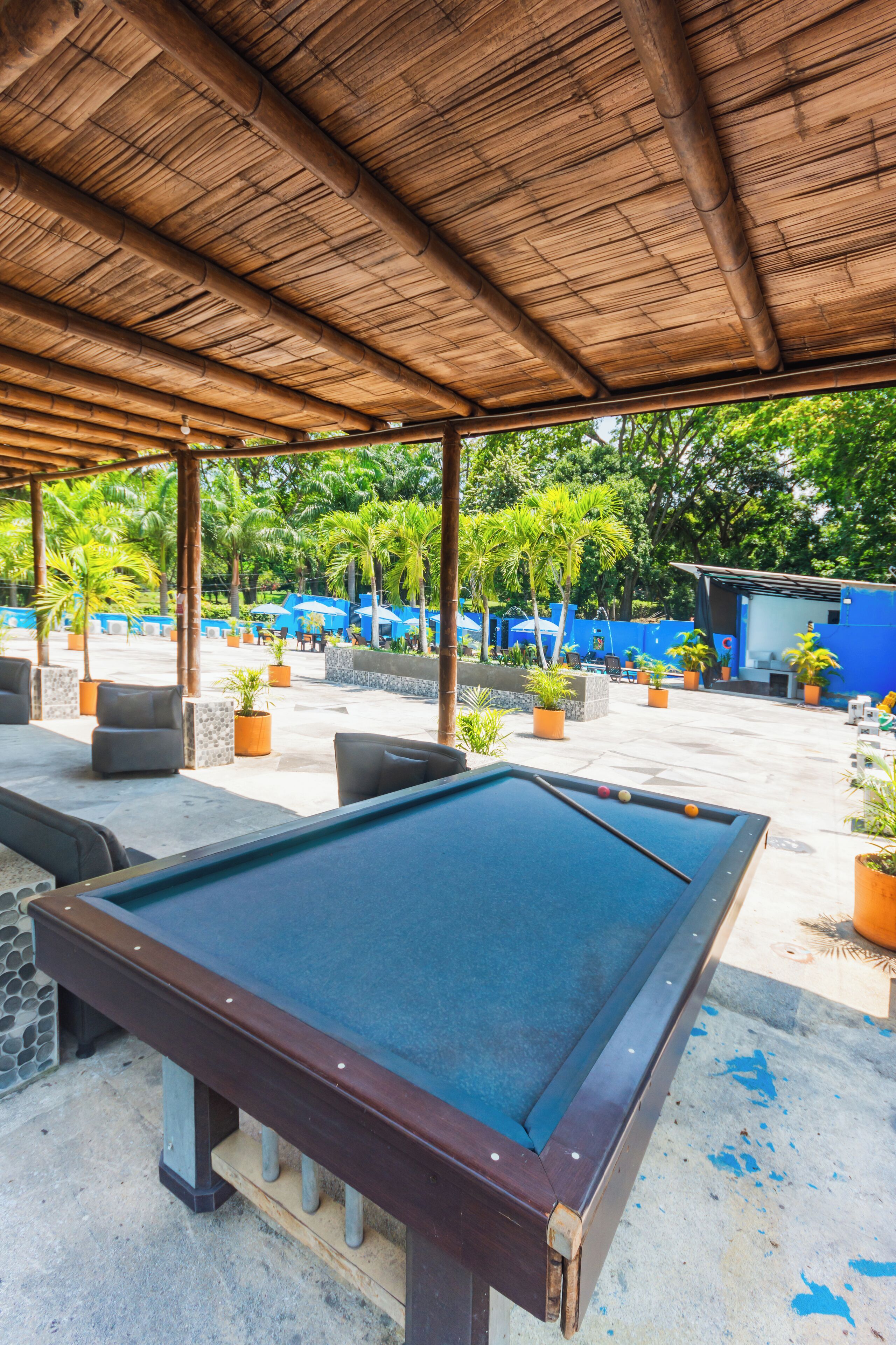 A pool table under a wooden roof with outdoor seating and potted plants.