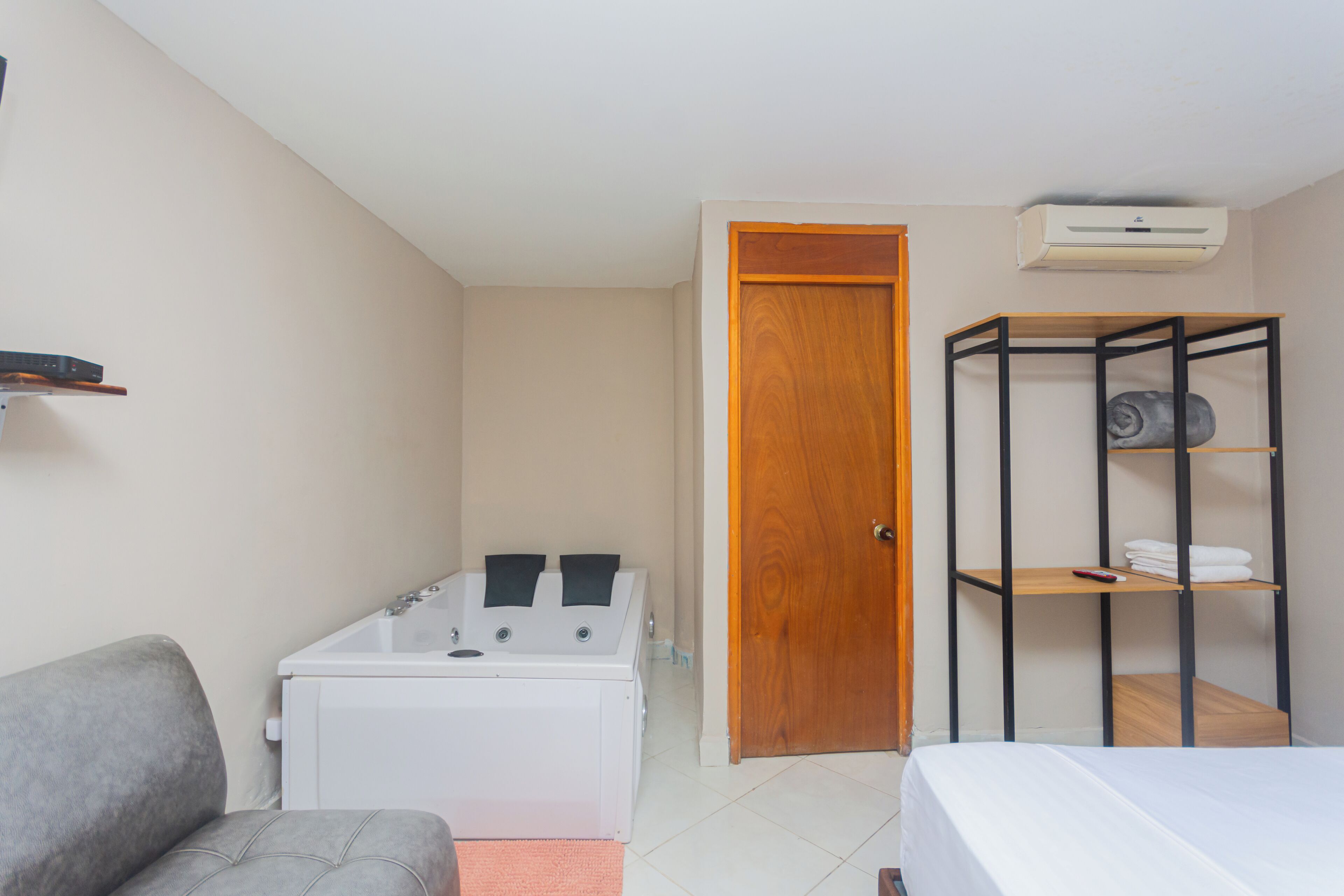 Una habitación compacta con una cama, un sofá, lavadora, un armario de madera y una estantería metálica.